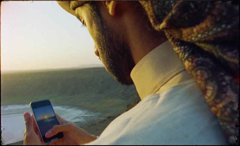 Man with an iphone photographing a natural area of a valley with a lake and the sun on the horizon