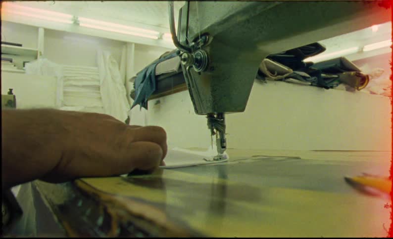 A pair of hands carefully guides fabric through a large industrial sewing machine