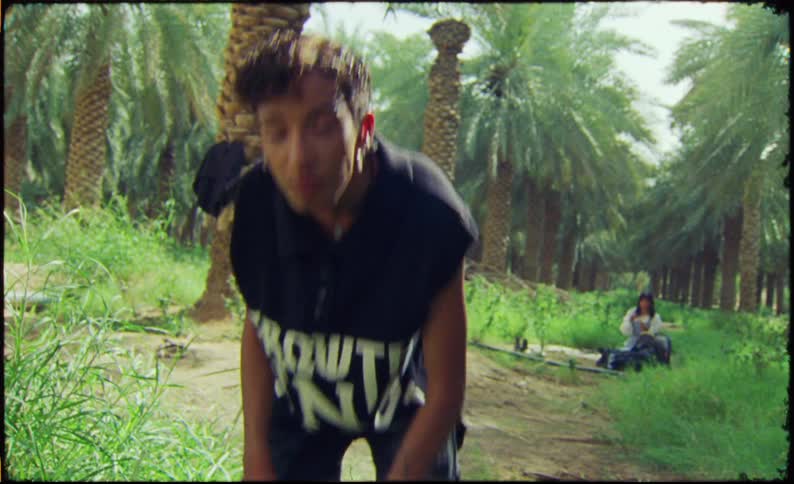 Young man fixing his hair while standing in a rainforest with a woman sitting in the background