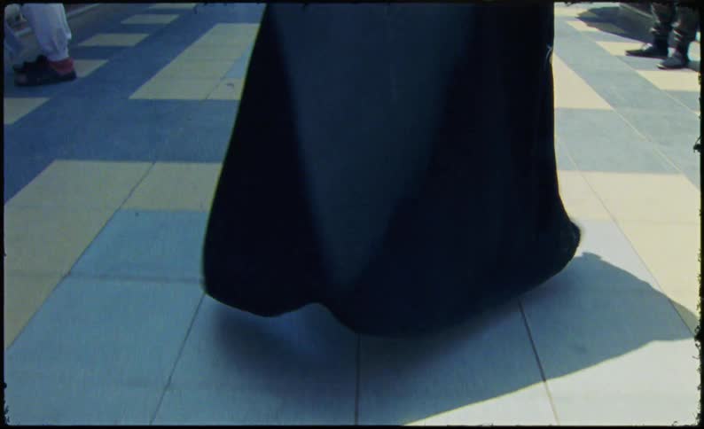 A woman in a black burka is walking through an outdoor market with various stalls selling clothing under colorful canopies