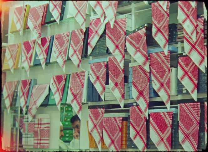 A shop window displays a vibrant array of red and white checkered keffiyehs neatly arranged in rows