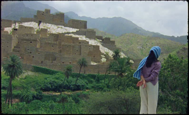 Woman with a headscarf in a tropical natural area with ruins on a hill in the background