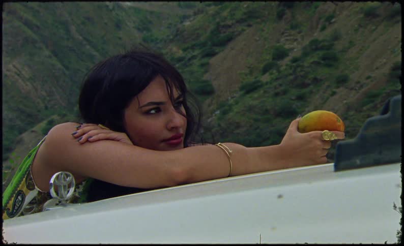 Woman in a sea outside with mountains in the background holding a fruit