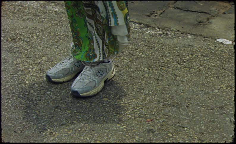 The feet of a person wearing white sneakers and a green dress are standing on a concrete floor