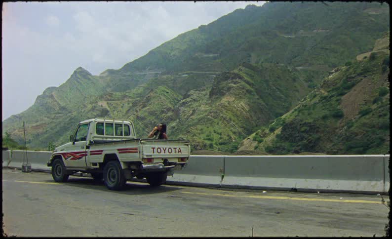 Woman standing next to a small truck on the road and a mountain valley in the background