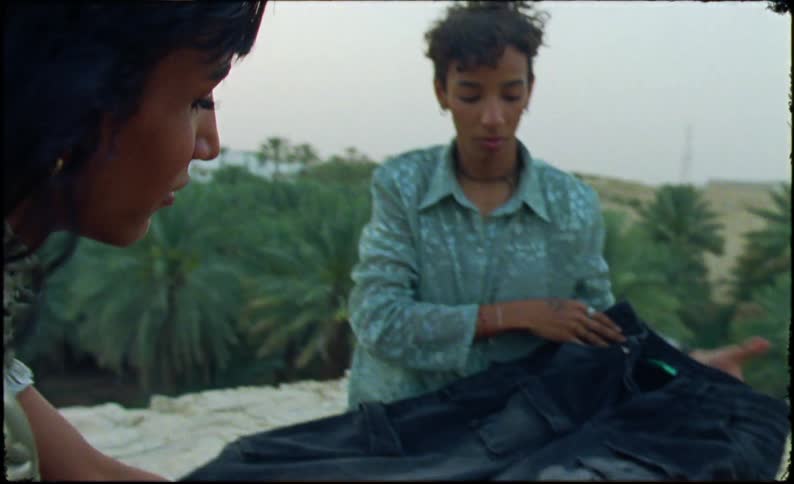 Two people sitting together in a natural area looking at a white piece of clothing