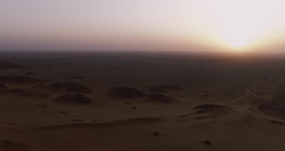 An aerial view of a large desert with many dunes and the sun is slowly setting