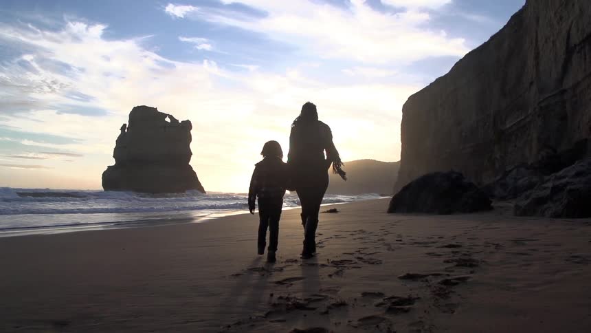 Child and adult hold hands walking down a beach at sunrise