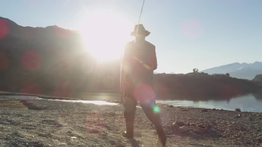 Man walks on the rocks by the water carrying a fishing pole