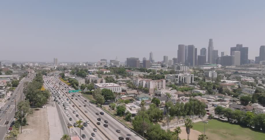 An aerial view of a large highway full of cars and further ahead are the buildings of a metropolitan city