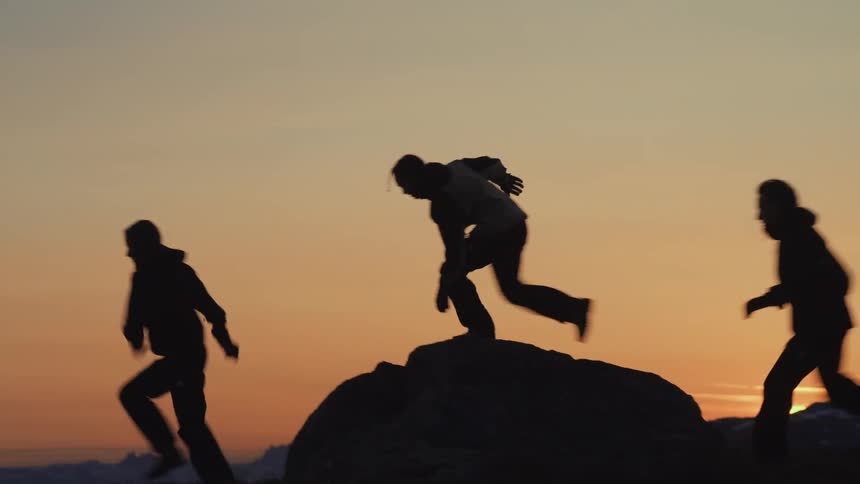 Three people running in the field are silhouetted against the sky at sunset