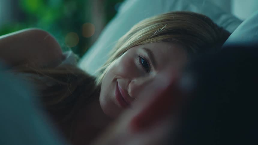A blonde woman and a man lie in bed looking at each other with love in the bedroom