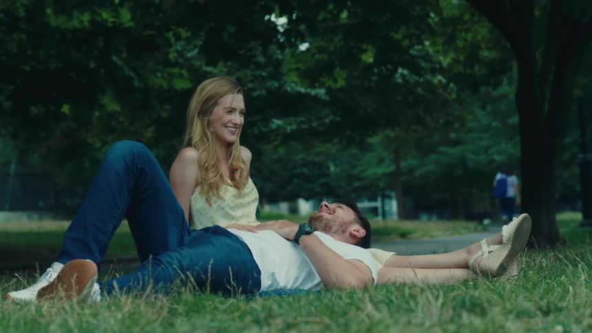 Woman sitting on grass in a park with a man lying on her legs