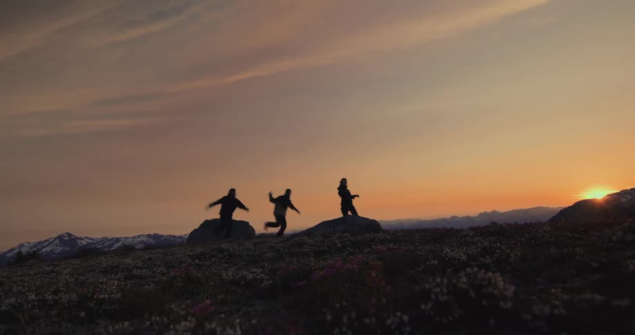 Silhouette of three people running across rocks in a natural mountain environment with the sunrise on the horizon