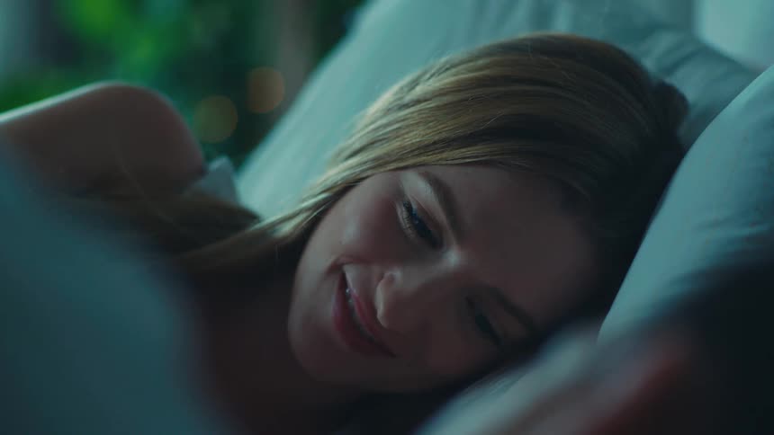Portrait of a young blonde woman lying in bed smiling with a man