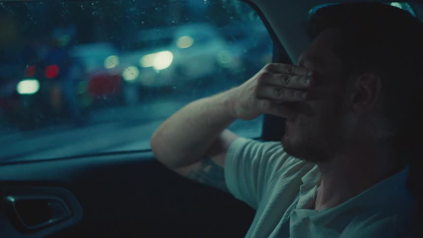 Man in the back seat of a car rubbing his eyes