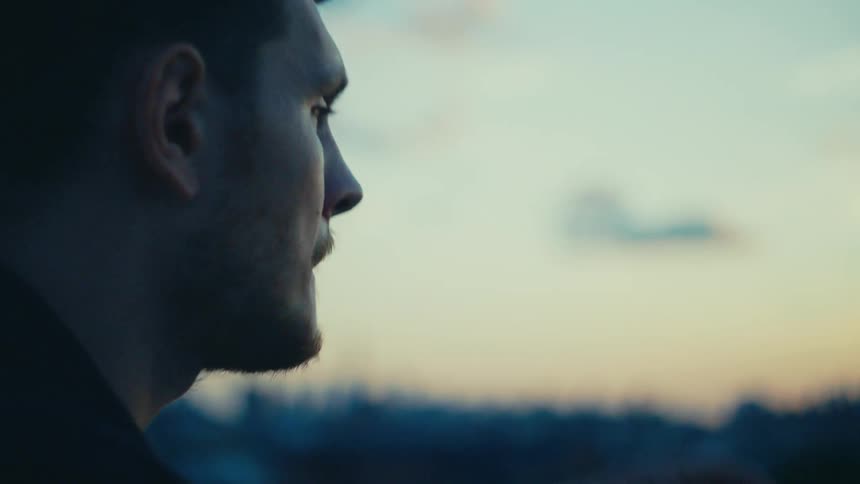 A man on a rooftop his fingers tapping away on a smartphone against the backdrop of a city skyline