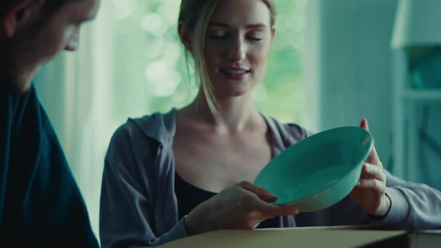 Blonde woman smiles while discussing bowl she just unpacked with a male friend