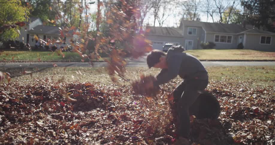 A brother and sister are playing in autumn leaves on a partly sunny day