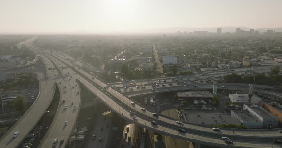 A hazy aerial view of a major highway interchange in los angeles with heavy traffic and a distant skyline