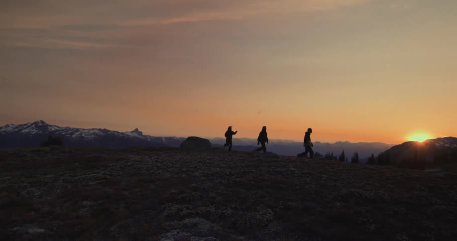 Three people are walking in mountainous terrain at sunset
