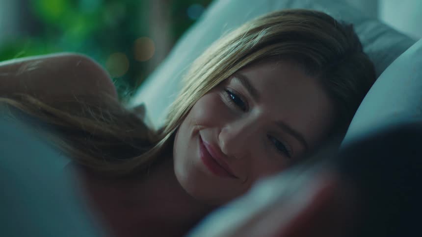 Portrait of a young blonde woman lying in bed with another person