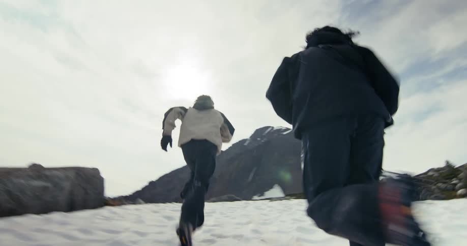 Two men race across the snow towards a hill on a cloudy winter day
