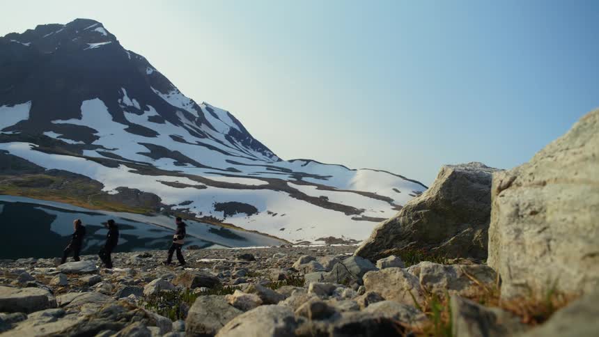 Three people are hiking across a rocky terrain with a snowcapped mountain in the background