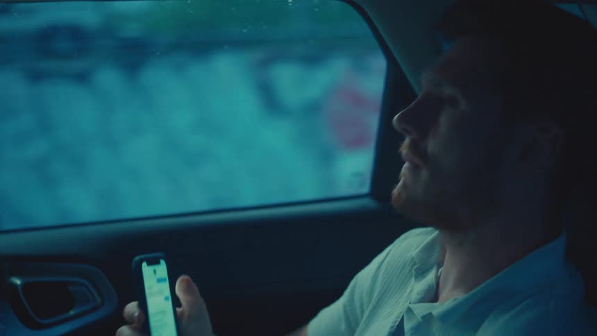 A man riding in a car reacts sadly to his phone