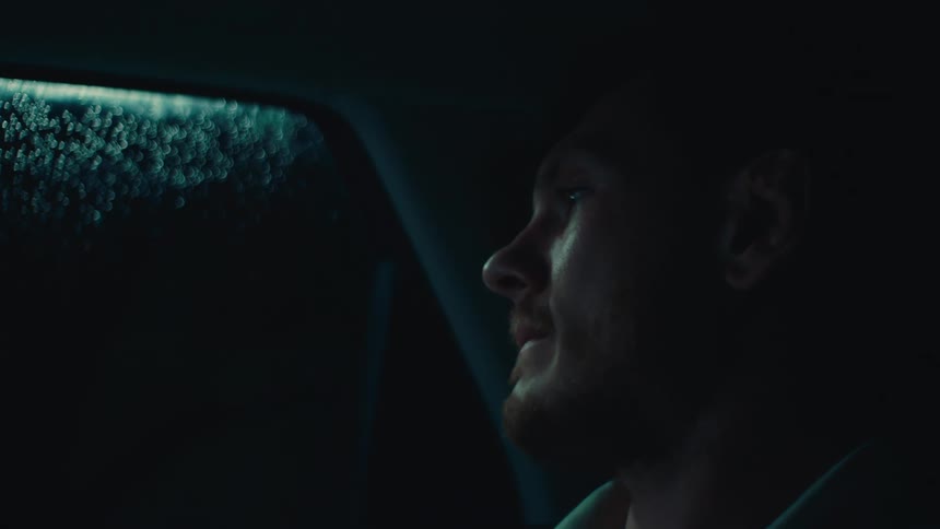 A pensive man sits in a car driving at night