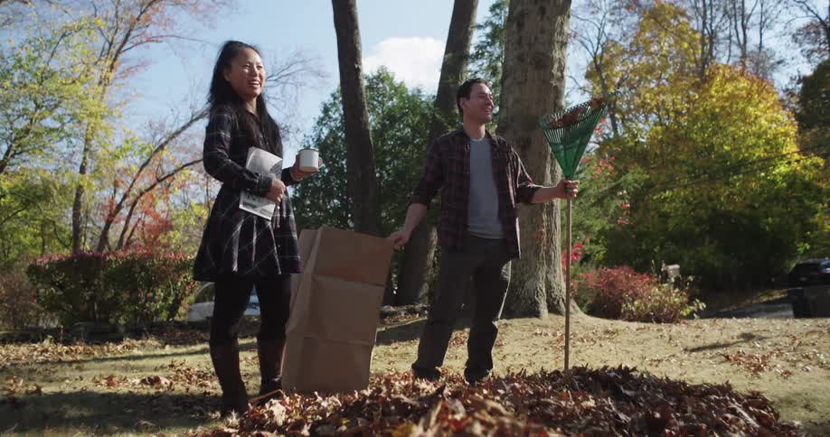 Man and a woman in a yard next to a cardboard box with dry leaves