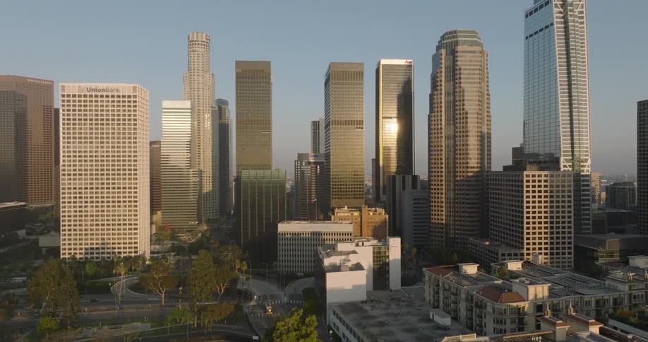 A cityscape featuring a cluster of modern skyscrapers with reflective glass facades set against a blue clear sky