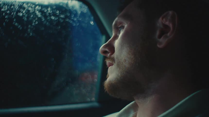 A man in a car observes the night scenery through the window surrounded by the dim light of the urban landscape