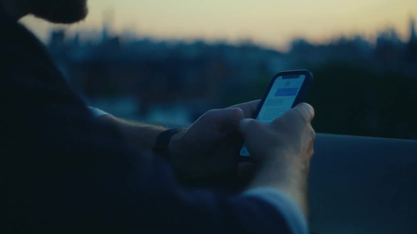 A persons hands typing a message on a smartphone with a blurred city skyline in the background