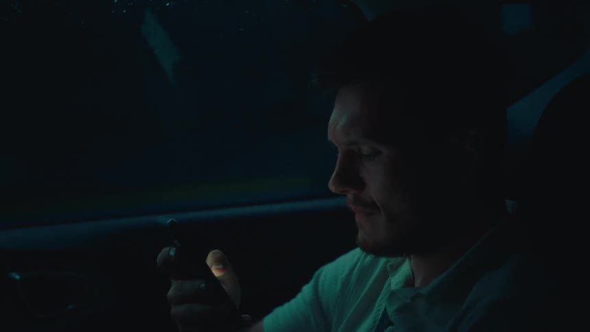 Side portrait of a man inside a moving car interacting with a smartphone
