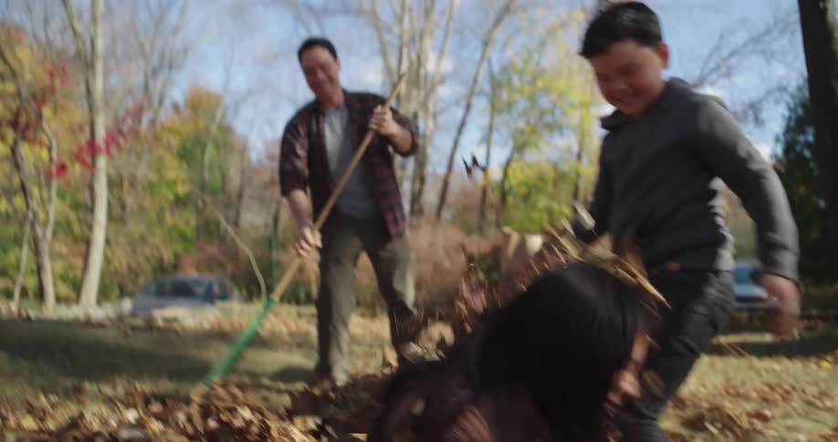 Father playing with his two children with dry leaves in the backyard