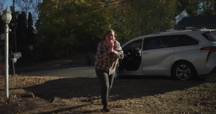 A grandma gets out of her car as her two grandkids excitedly run up and hug her