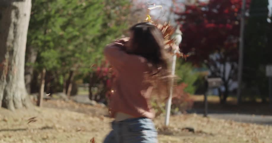 Girl playfully throwing leaves from a pile in the front yard