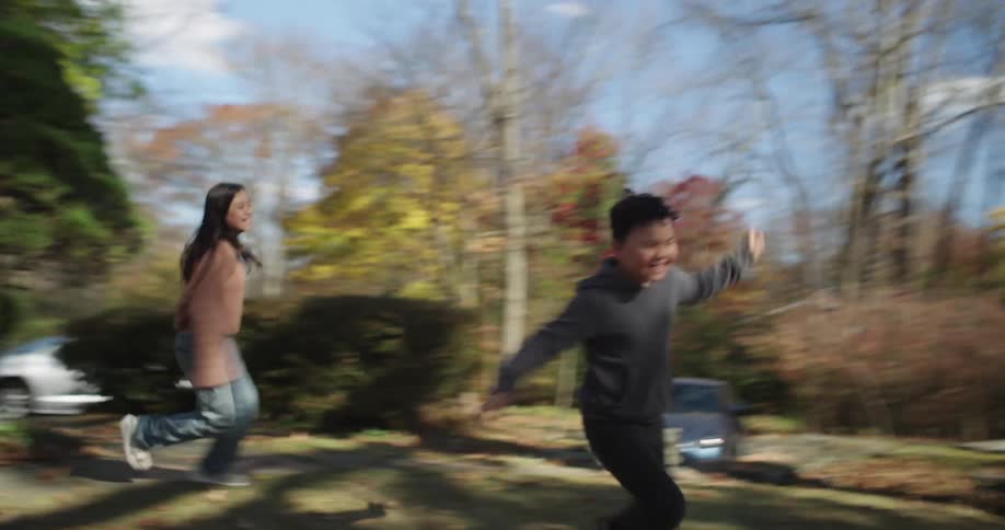 Two children running in the yard towards dry leaves