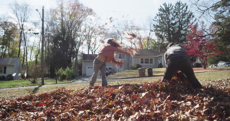 Two young children throw leaves at each other on a clear fall day