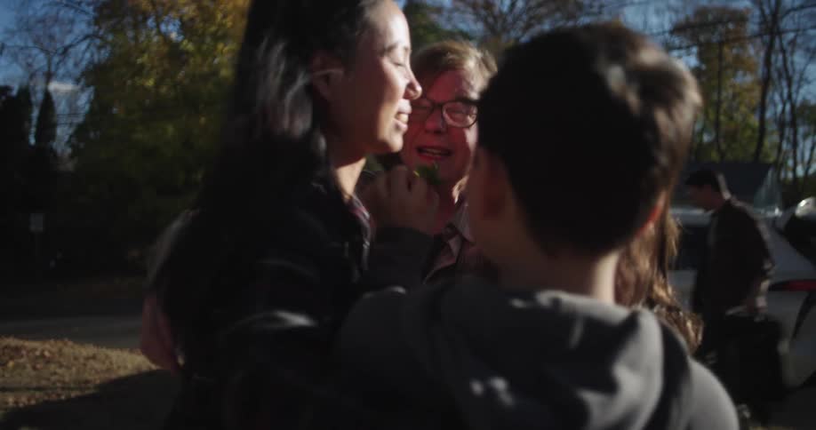 A heartfelt embrace among an elderly woman andthree children outdoors with a car and autumn trees in the background