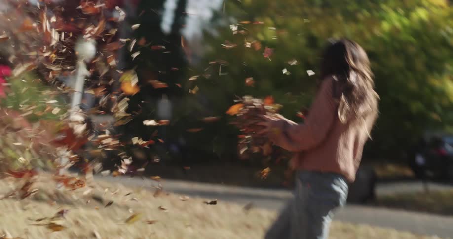 A boy and a girl playfully toss and throw piles of autumn leaves in a yard