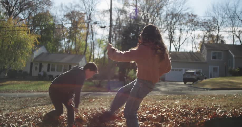 A brother and sister play in autumn leaves on a partly sunny day