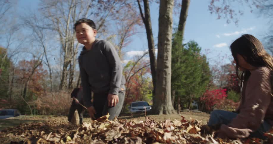Son and daughter play with autumn leaves while the father rakes in the yard