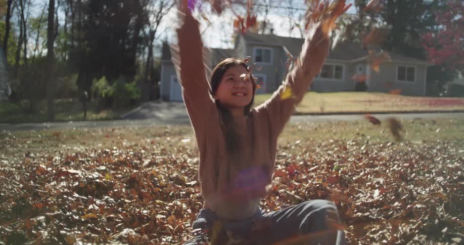 Girl sitting in a backyard of a house playing with dry leaves