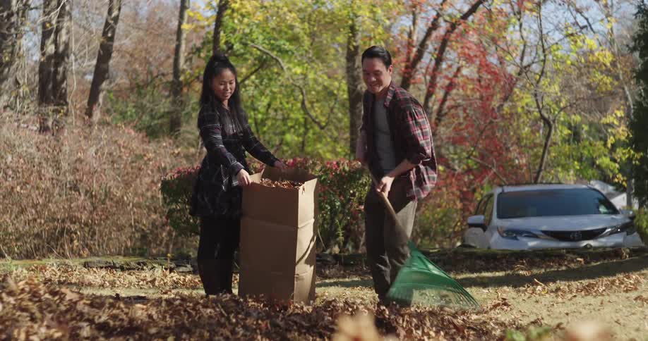 Woman holding a cardboard box while a man dumps dry leaves and in the foreground legs of children running
