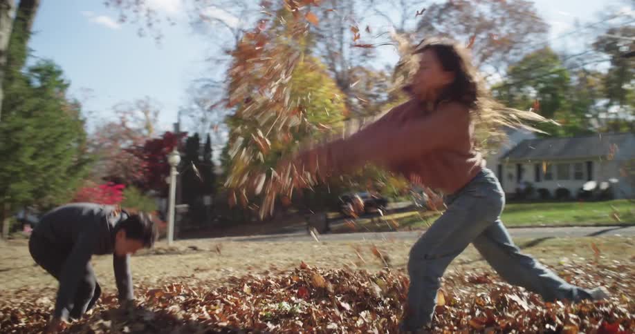 Man cleaning a yard and his two children playing with dry leaves