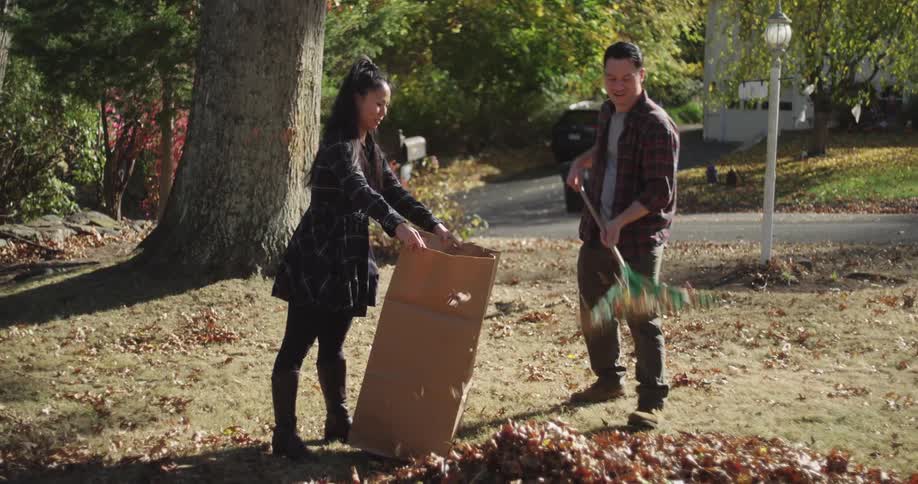 Woman holding a cardboard bag and a man putting dry autumn leaves