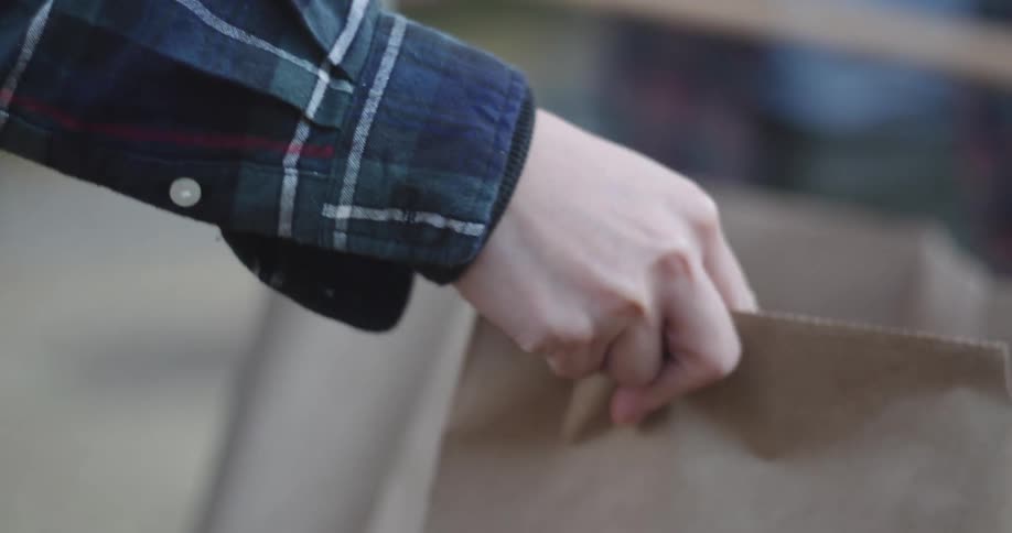 Hand holding a cardboard bag and another person pouring dry leaves inside