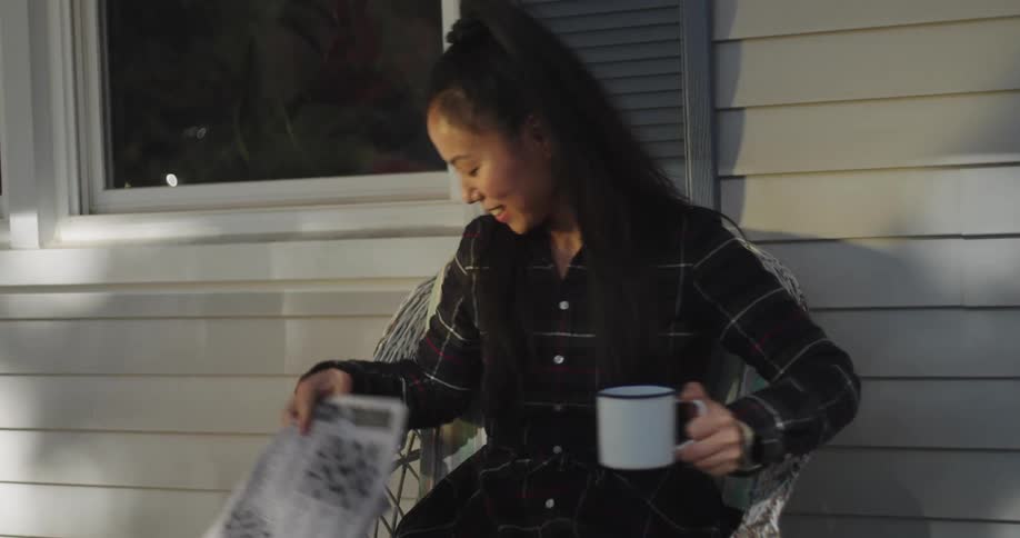 Woman drinking coffee and reading the newspaper when two children walk in front of her and she stands up smiling